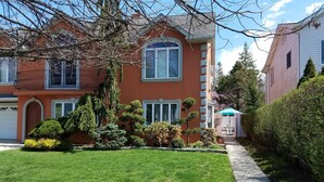 A two-story house with a well-maintained lawn, a small garden with various shrubs, and a clear sky. - Secluded, Sunny Studio.  Fully Private: entrance, bath, bedroom, kitchen & Patio (Valley Stream)