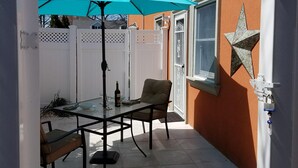 A patio with a table and chairs, a blue umbrella, and a decorative star on the wall. - Secluded, Sunny Studio.  Fully Private: entrance, bath, bedroom, kitchen & Patio (Valley Stream)