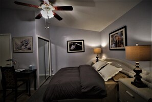 A bedroom with a bed, a desk, a chair, a ceiling fan, and framed pictures on the walls. - Secluded, Sunny Studio.  Fully Private: entrance, bath, bedroom, kitchen & Patio (Valley Stream)