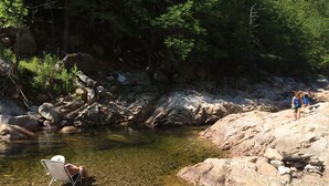 Un argine roccioso con acqua limpida, una sedia e due persone che camminano.
