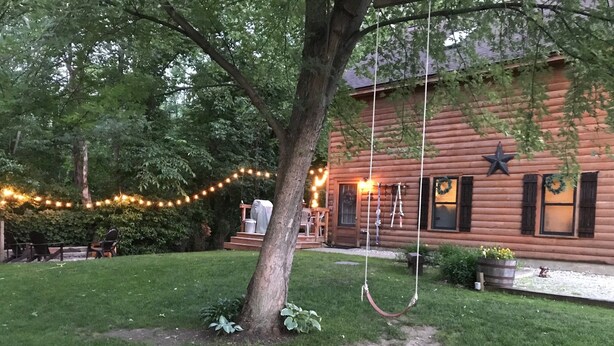 Un rustico chalet in legno con veranda, luci decorative e un'altalena appesa a un albero.