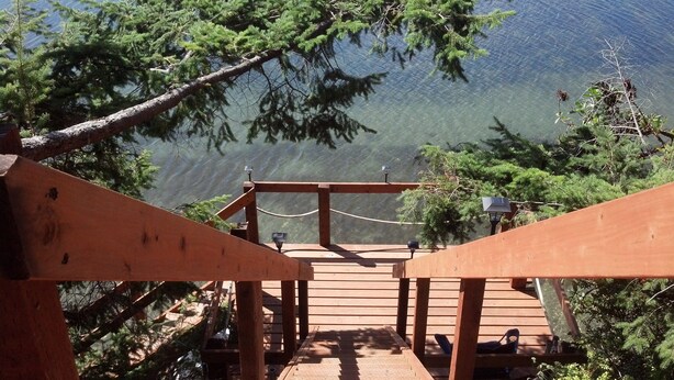 Une terrasse en bois, entourée d’une clôture en treillis métallique, qui offre une vue sur un lac bordé d’arbres.