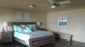 Une chambre à coucher avec un lit en bois, deux tables de chevet, un ventilateur de plafond et une fenêtre donnant sur un beau paysage.
