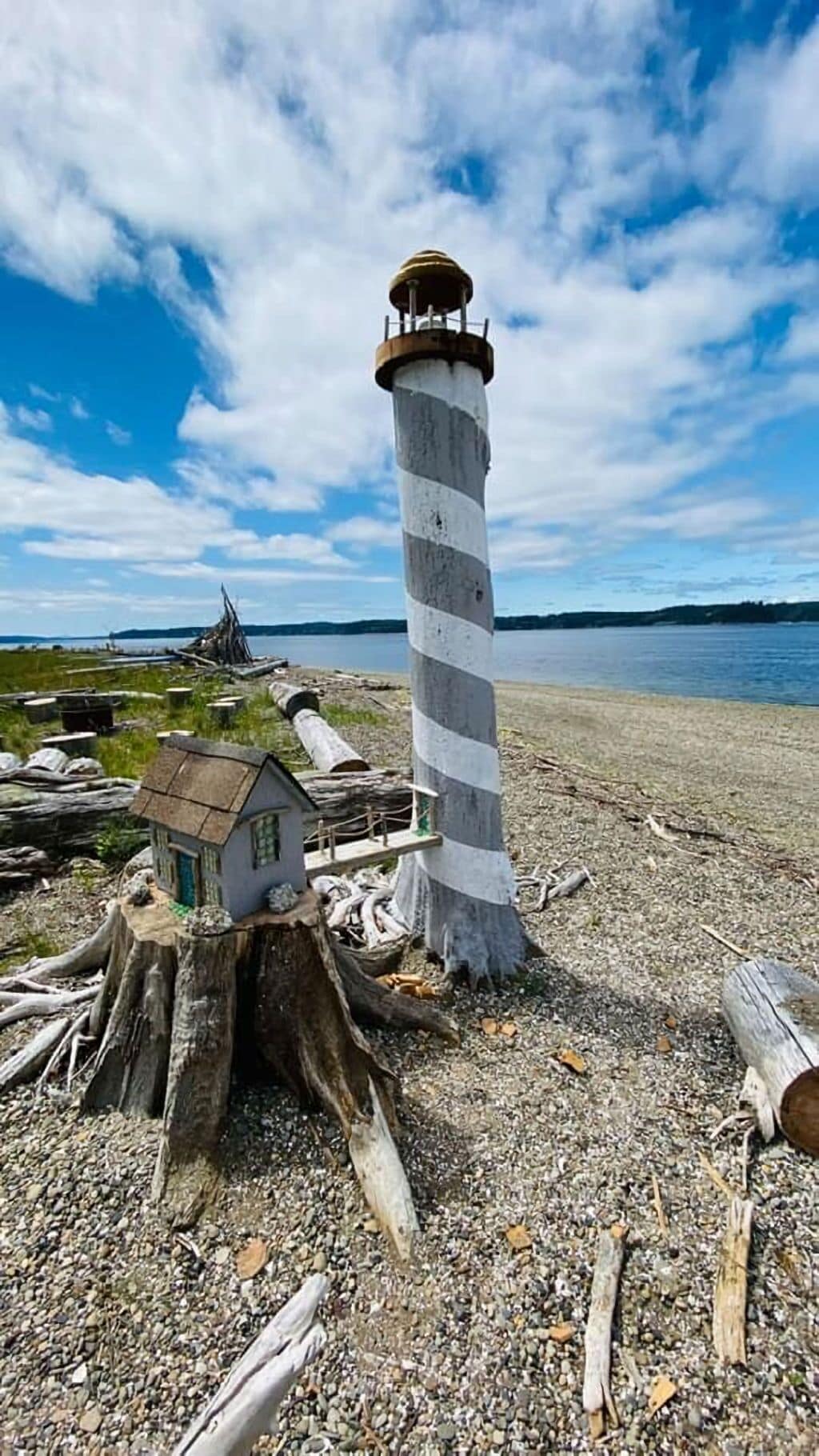 Un phare aux motifs rayés, situé sur une côte rocheuse, avec un petit bâtiment à proximité.