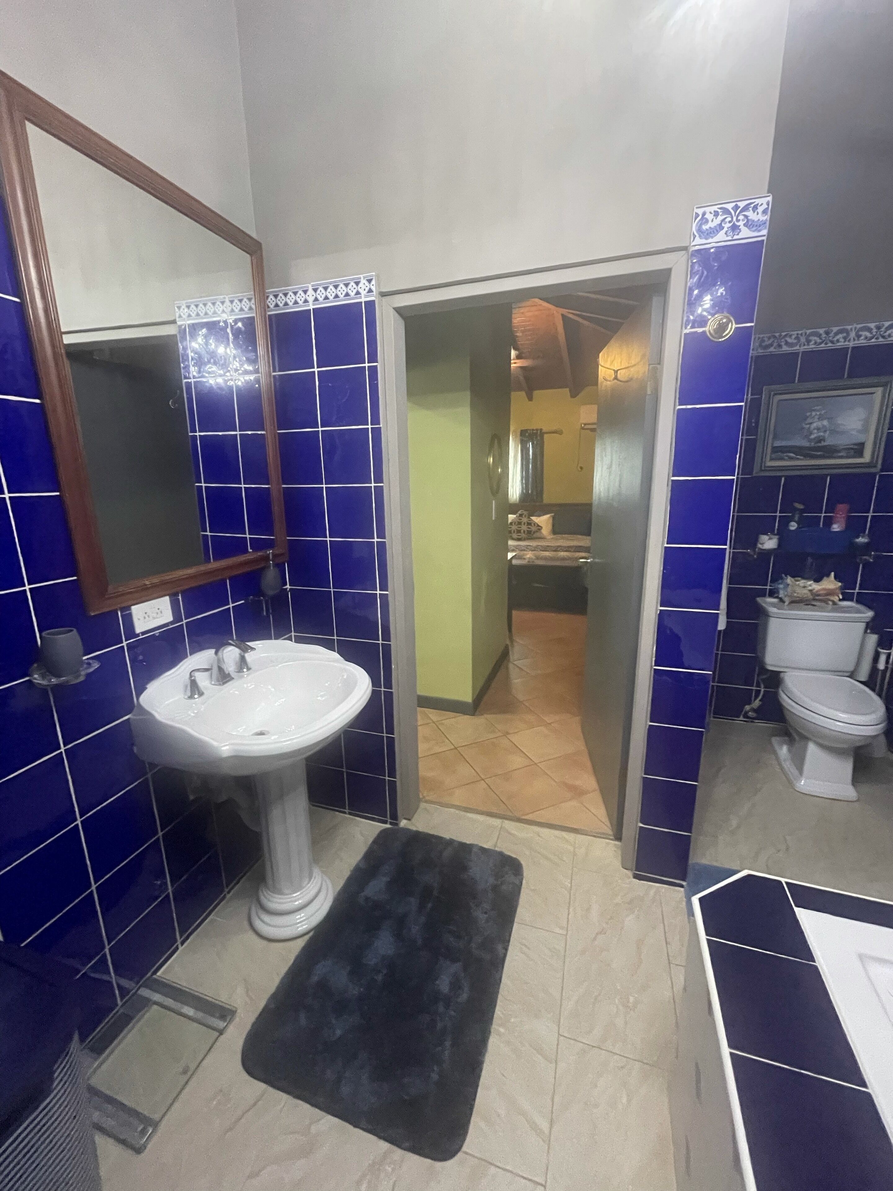 Ein Badezimmer mit einem weißen Waschbecken, blauen Fliesen, einem schwarzen Teppich und einer Toilette.