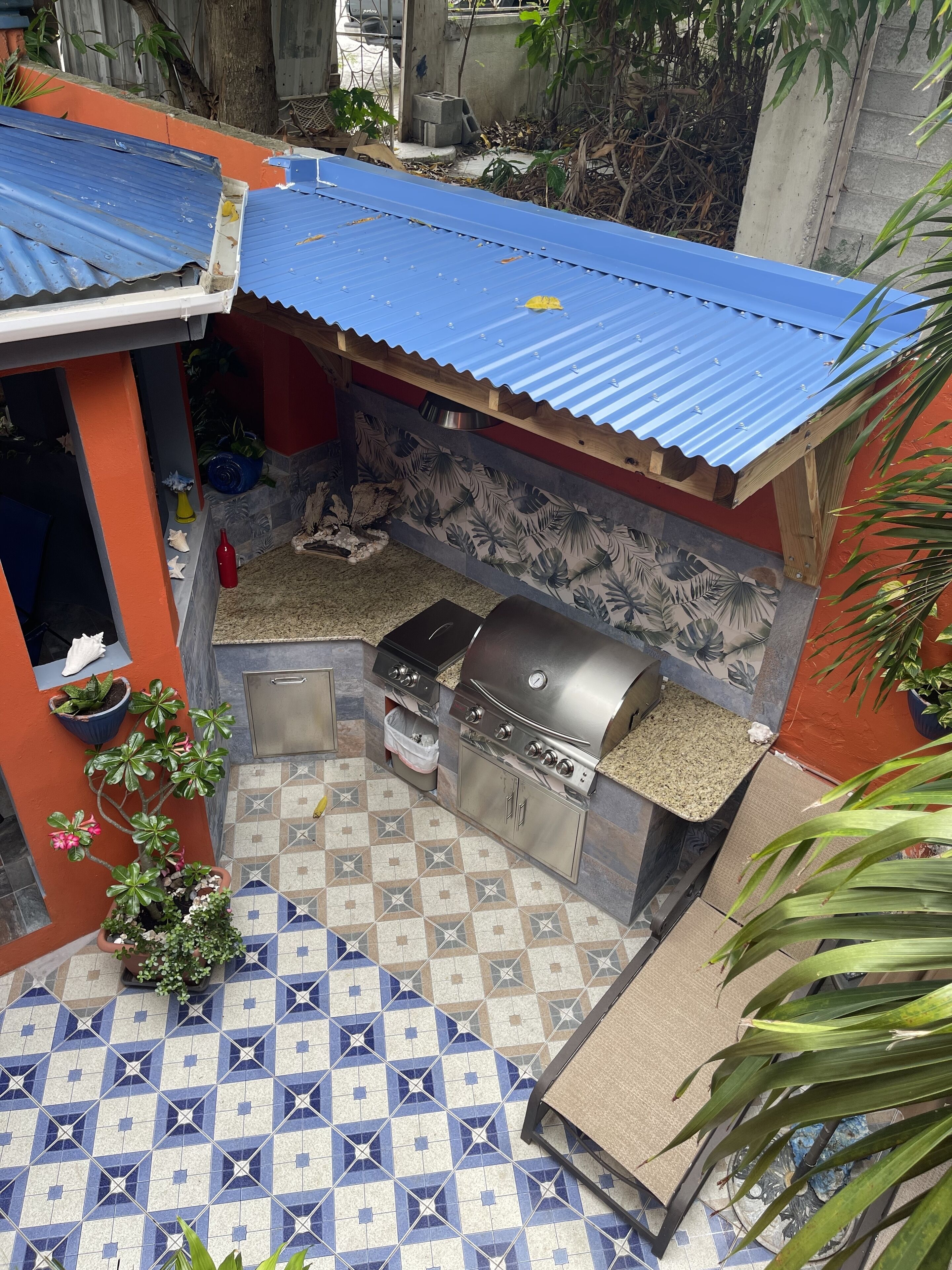 Een terras met een barbecue, betegelde vloer en potplanten.