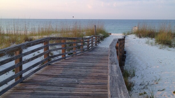 A wooden boardwalk leading to a beach with sand and sparse vegetation. - Perdido Key Waterfront Home with boat dock, canal, Gulf right across the street (Pensacola)