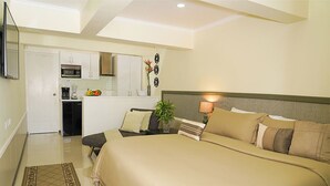 A bedroom with a large bed, bedside table, lamp, and a view of the kitchen. - Luxury Palm Beach Suite 5mins Away Walkable from the Beach & Marriott Hotel (Aruba)