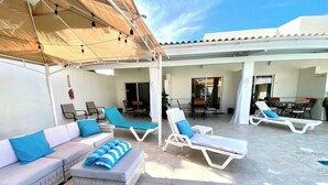 A covered outdoor lounge area with seating and tables, a fire extinguisher, and a view of the interior. - Luxury Palm Beach Suite 5mins Away Walkable from the Beach & Marriott Hotel (Aruba)