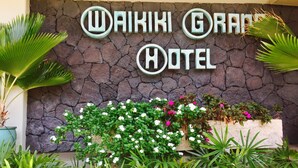 A sign for Waikiki Grand Hotel with a stone wall backdrop and lush greenery in front. - Amazing Diamond Head and Ocean Views, Prime Location-Free High Speed Wifi (Honolulu)