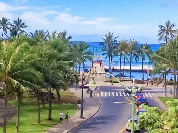A street with palm trees, a pedestrian crossing, and a view of the ocean. - Amazing Diamond Head and Ocean Views, Prime Location-Free High Speed Wifi (Honolulu)