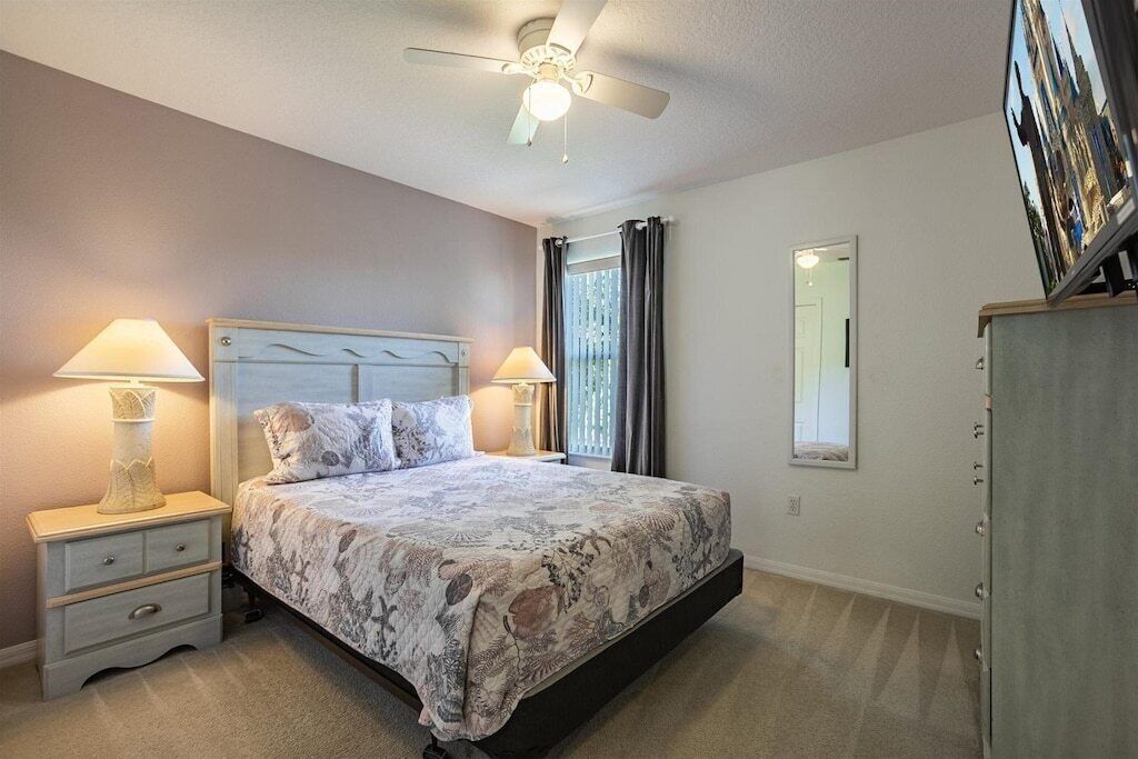 A bedroom with a bed, nightstands, a ceiling fan, a window with curtains, and a mirror on the wall.