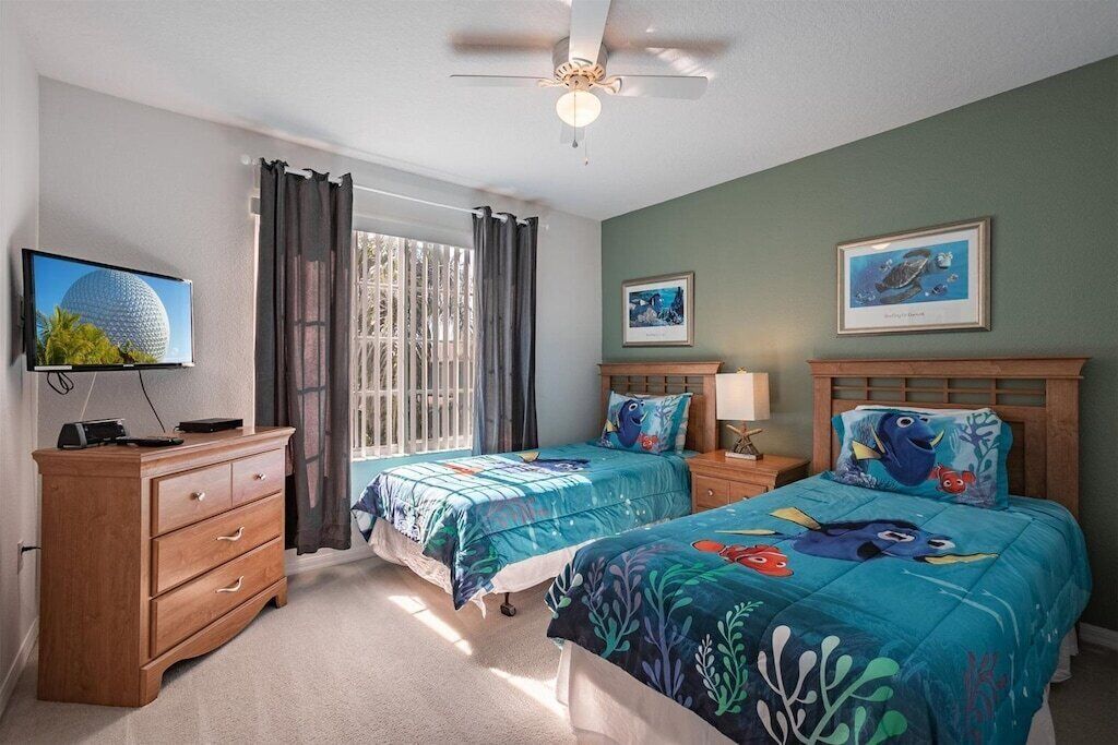 A bedroom with two beds, a TV, a dresser, and a ceiling fan.
