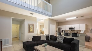 A spacious living area with a dark-colored sectional sofa, a coffee table, and a kitchen in the background. - Near Disney, Upscale 5 BR 2 Story Pool Home w/ game room (Davenport)
