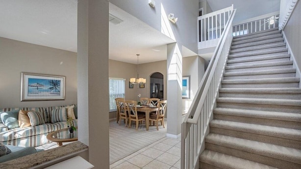 A spacious living area with a sofa, coffee table, and dining table. A staircase leads to an upper level. - Near Disney, Upscale 5 BR 2 Story Pool Home w/ game room (Davenport)