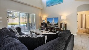 A living room with a large window, a sofa, a coffee table, and a TV. - Near Disney, Upscale 5 BR 2 Story Pool Home w/ game room (Davenport)