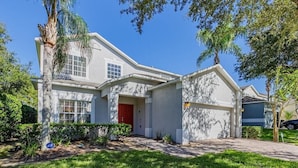 A two-story house with a red door, a garage, and a well-maintained lawn. - Near Disney, Upscale 5 BR 2 Story Pool Home w/ game room (Davenport)
