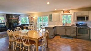 A modern kitchen with white cabinets, a dining area with wooden chairs, and a stone fireplace. - Spacious 6BR - 5BA Ski Home on Pico Mountain - Minutes to Killington Mountain (Killington)