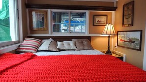 Een slaapkamer met een groot bed, een raam met uitzicht op boten, een lamp en ingekaderde foto's aan de muur.