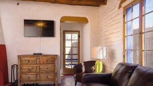 Un salon chaleureux avec un canapé en cuir, une commode en bois et un téléviseur fixé au mur.