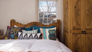 Une chambre avec un lit en bois, des coussins colorés, une fenêtre et une armoire en bois.