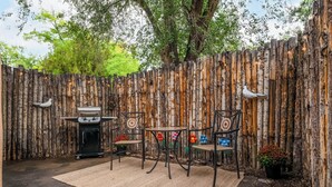 Une terrasse extérieure agrémentée d’une clôture en bois rustique, d’un barbecue et de deux chaises au dossier décoratif.
