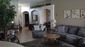 A living room with grey sofas, a coffee table, and a dining area with a table and chairs. There is a plant in the corner and artwork on the walls. - Luxury Pool Home Steps to Disney, 2 Master Suites, Gated, Game Rm, BBQ Free WiFi (Kissimmee)
