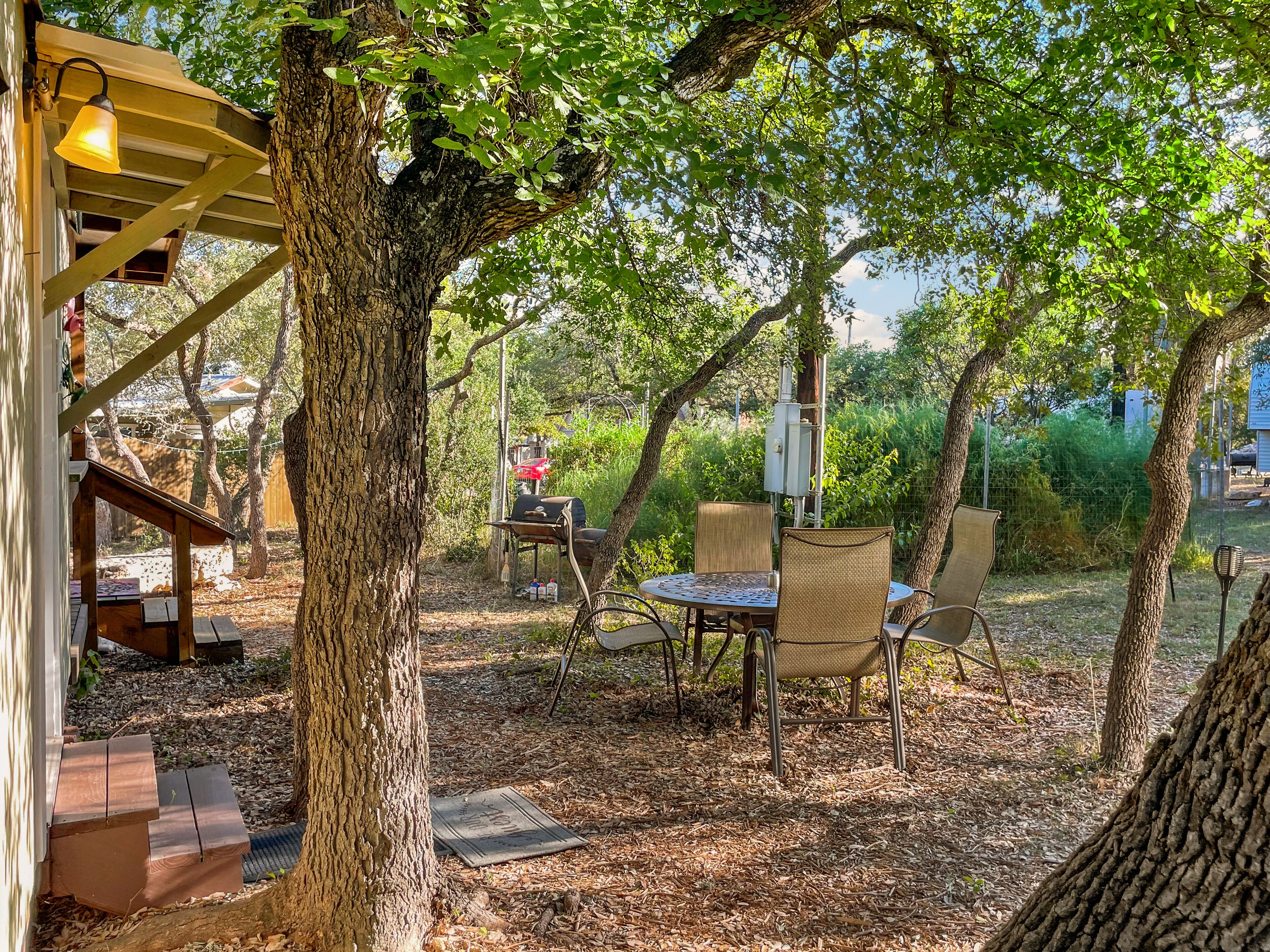 Un patio con mesa y sillas, rodeado de árboles y una pérgola de madera.