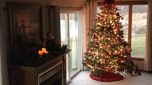Un salon avec une cheminée, un sapin de Noël et une grande fenêtre.