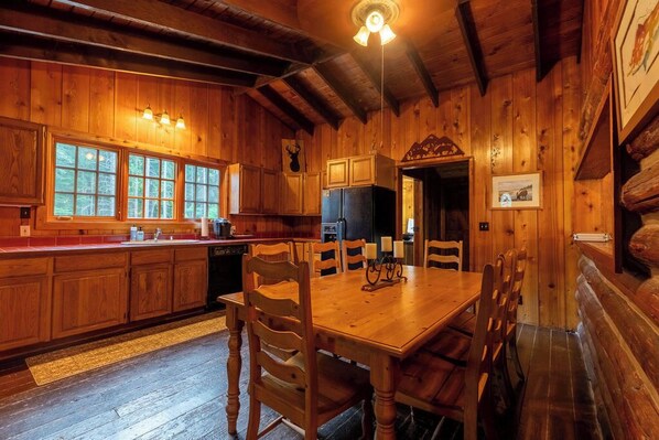 A wooden cabin interior with a dining area, kitchen, and large windows. - Two Beautiful Log Cabins alongside the Sol Duc River! (Beaver)