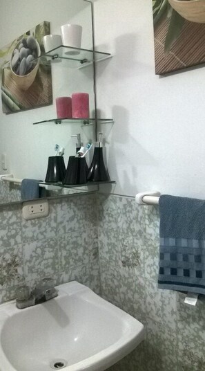 Uma casa de banho com uma pia branca, um espelho e uma prateleira de vidro com artigos de higiene pessoal.