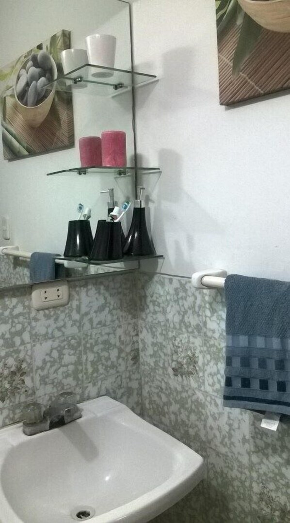 A bathroom with a white sink, a mirror, and a glass shelf holding toiletries.