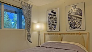 A bedroom with a bed, a bedside lamp, a window with a curtain, and two wall-mounted artworks. - Cozy Kirkland Finn Hill Home (Kirkland)