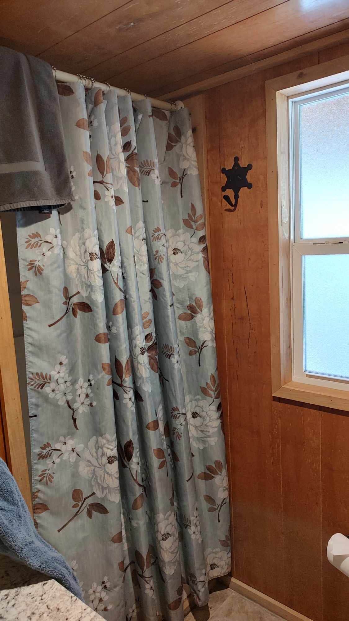 Een kamer met houten wanden, een raam met een witte kader en een gordijn met een bloemenprint.