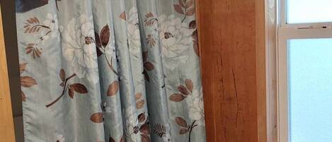 Een kamer met houten wanden, een raam met een witte kader en een gordijn met een bloemenprint.