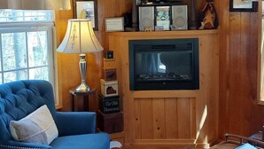 A cozy living room with a blue sofa, a fireplace, a flat-screen TV, and a clock on the wall.