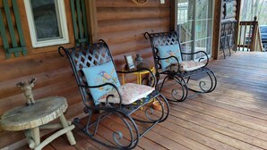 Two rocking chairs with floral cushions on a wooden deck of a log cabin.