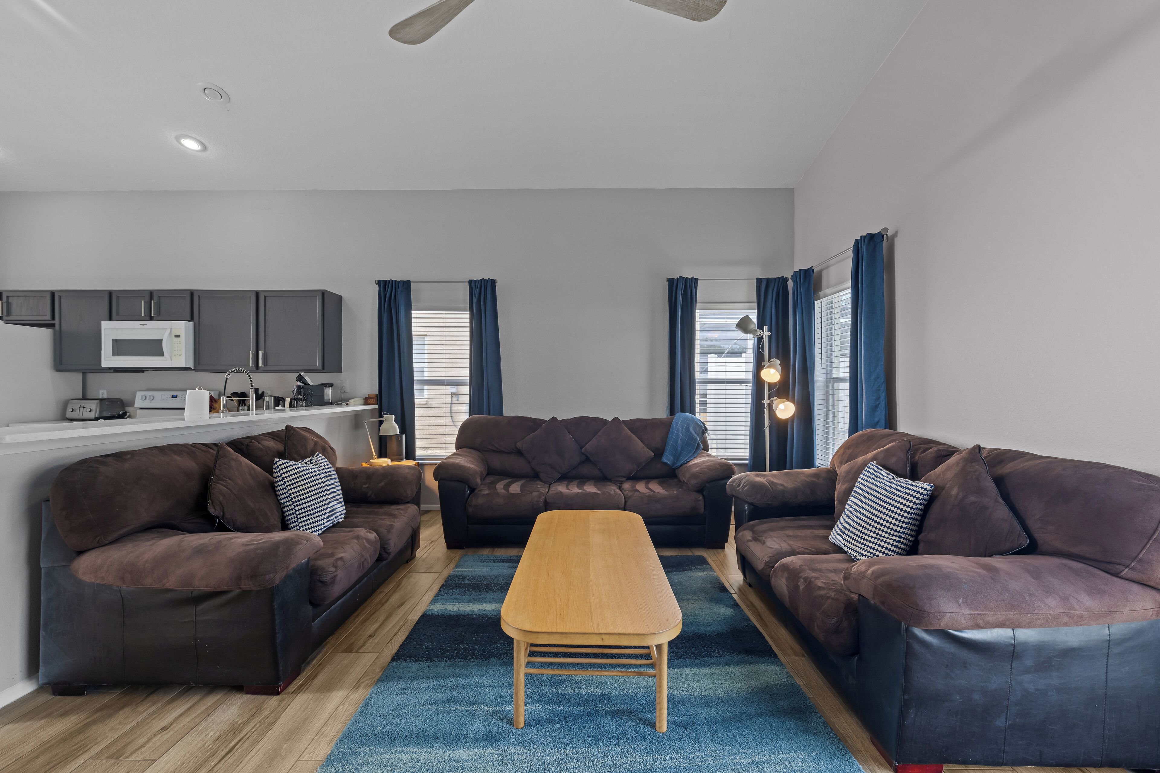 A modern living room with a brown leather sofa set, a wooden coffee table, and a kitchen area with a microwave.