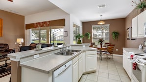 Una cocina moderna con una isla central, armarios blancos y una zona de comedor con mesa y sillas.