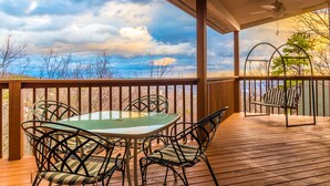 A covered outdoor area with a table and chairs, a swing, and a view of the sky and landscape.