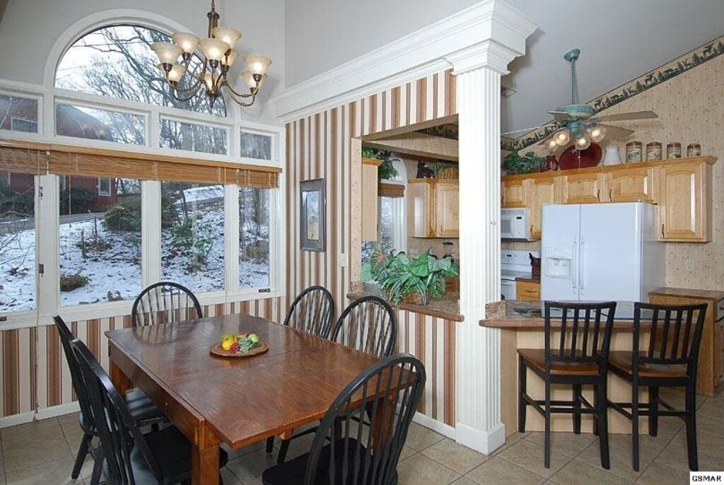 A dining area with a wooden table and chairs, a chandelier, and a view of a snowy landscape through large windows.