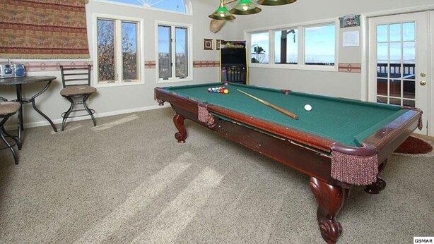 A pool table with balls, a ceiling fan, and a view of the outdoors through a window.