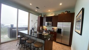 Una cucina moderna con una grande isola, sgabelli da bar, elettrodomestici in acciaio inossidabile e vista panoramica attraverso ampie finestre.