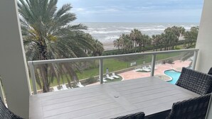 Un balcone con tavolo e sedie affacciato su una spiaggia e una piscina.