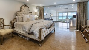 Un dormitorio espacioso con una cama grande, una zona de estar con una silla y vistas al océano a través de amplios ventanales.