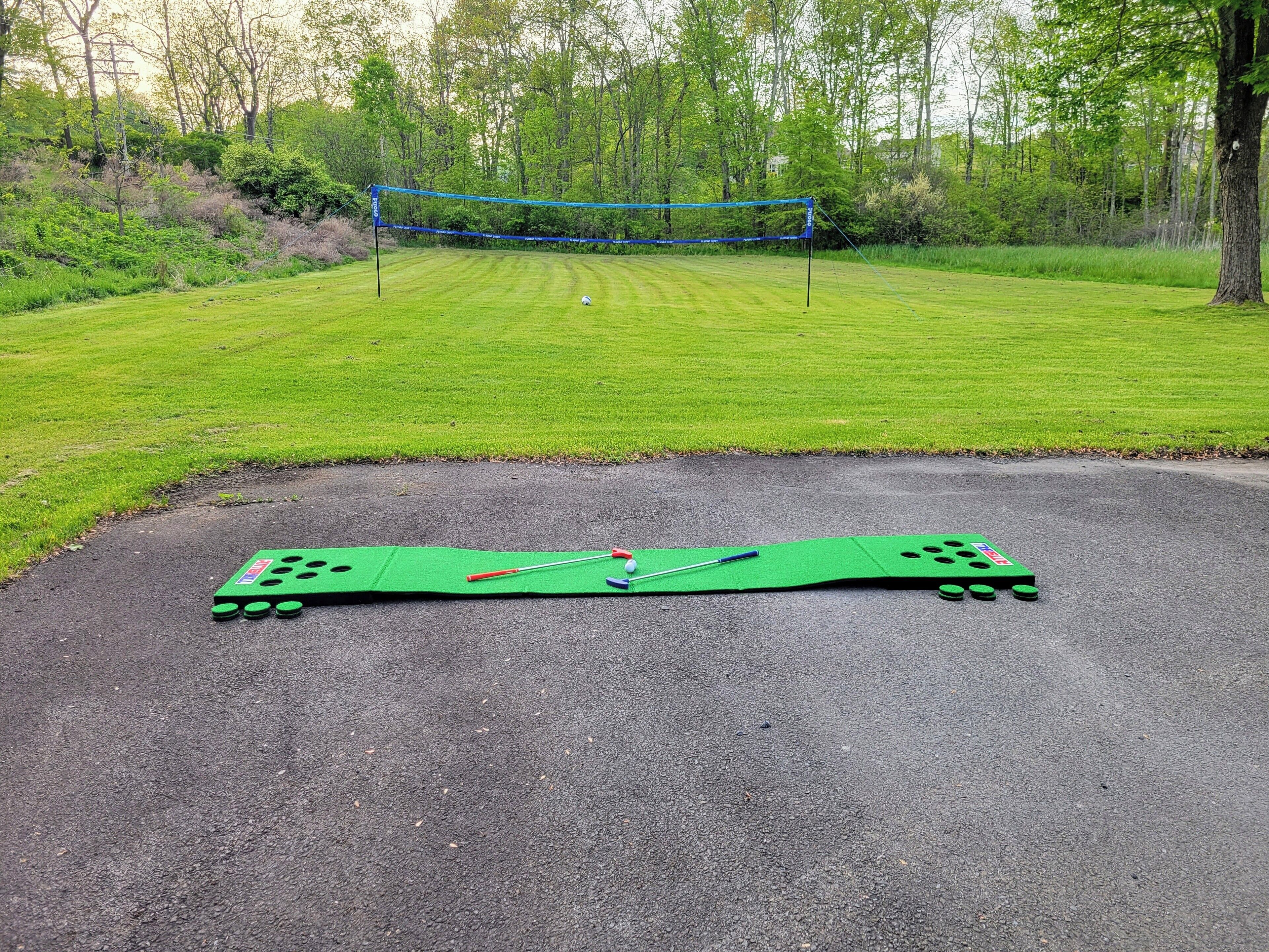 A green croquet mat on a paved surface with a netted area in the background.