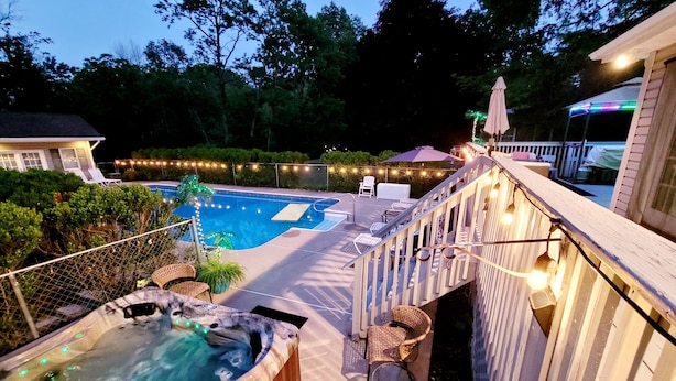 Un área de piscina con jacuzzi, sillas de descanso e iluminación festiva.