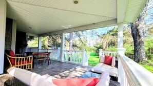 Un patio techado con muebles de mimbre y una mesa, con vistas a un jardín verde.