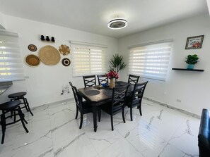 Un coin repas avec une table ronde, des chaises noires, un vase de fleurs et un luminaire au plafond.