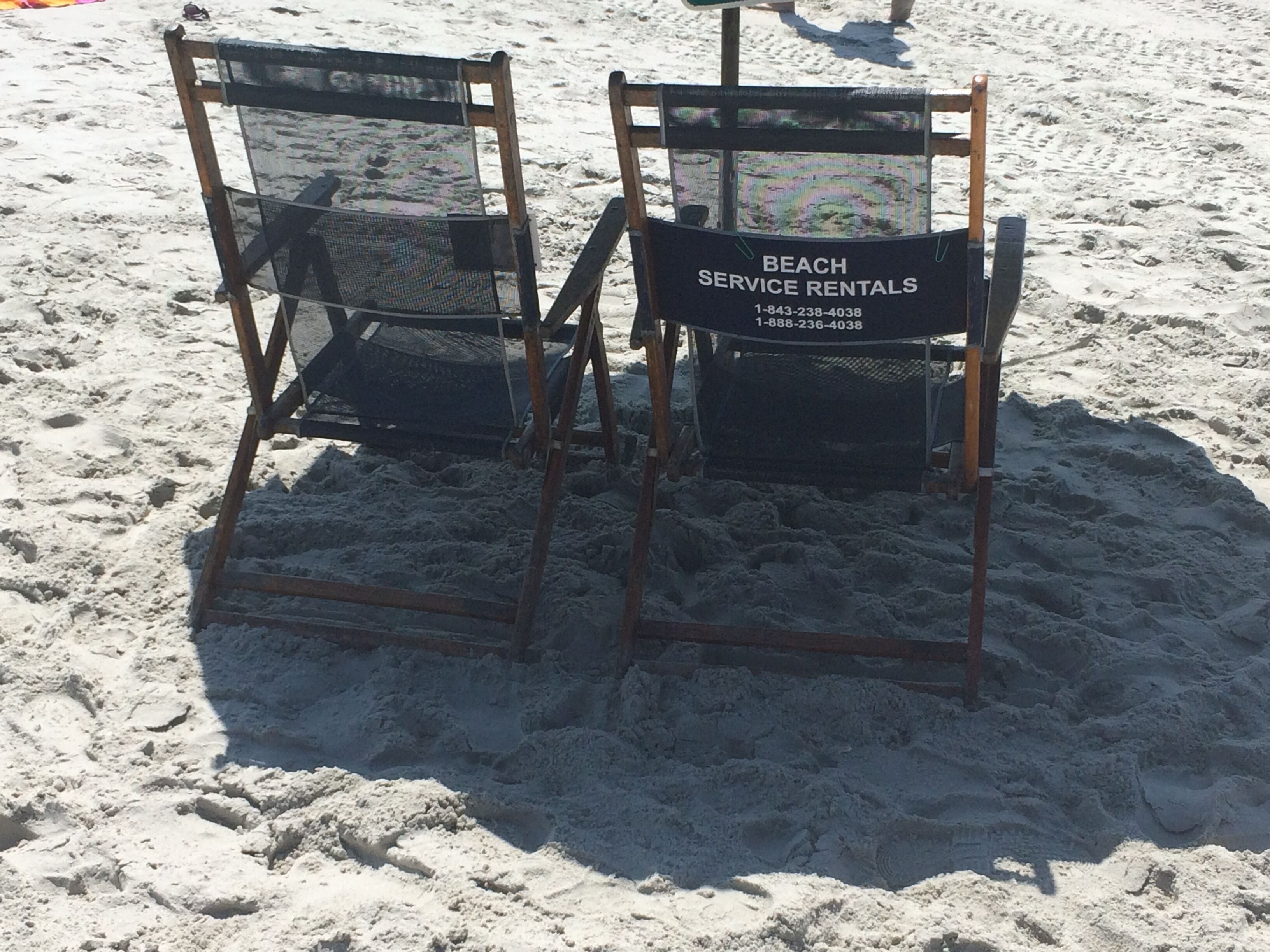 Two beach service rental chairs with a sign indicating beach service rentals and contact numbers.